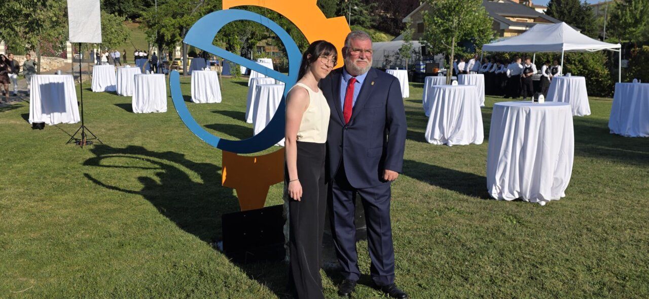 Dos personas posando en un evento al aire libre con mesas blancas