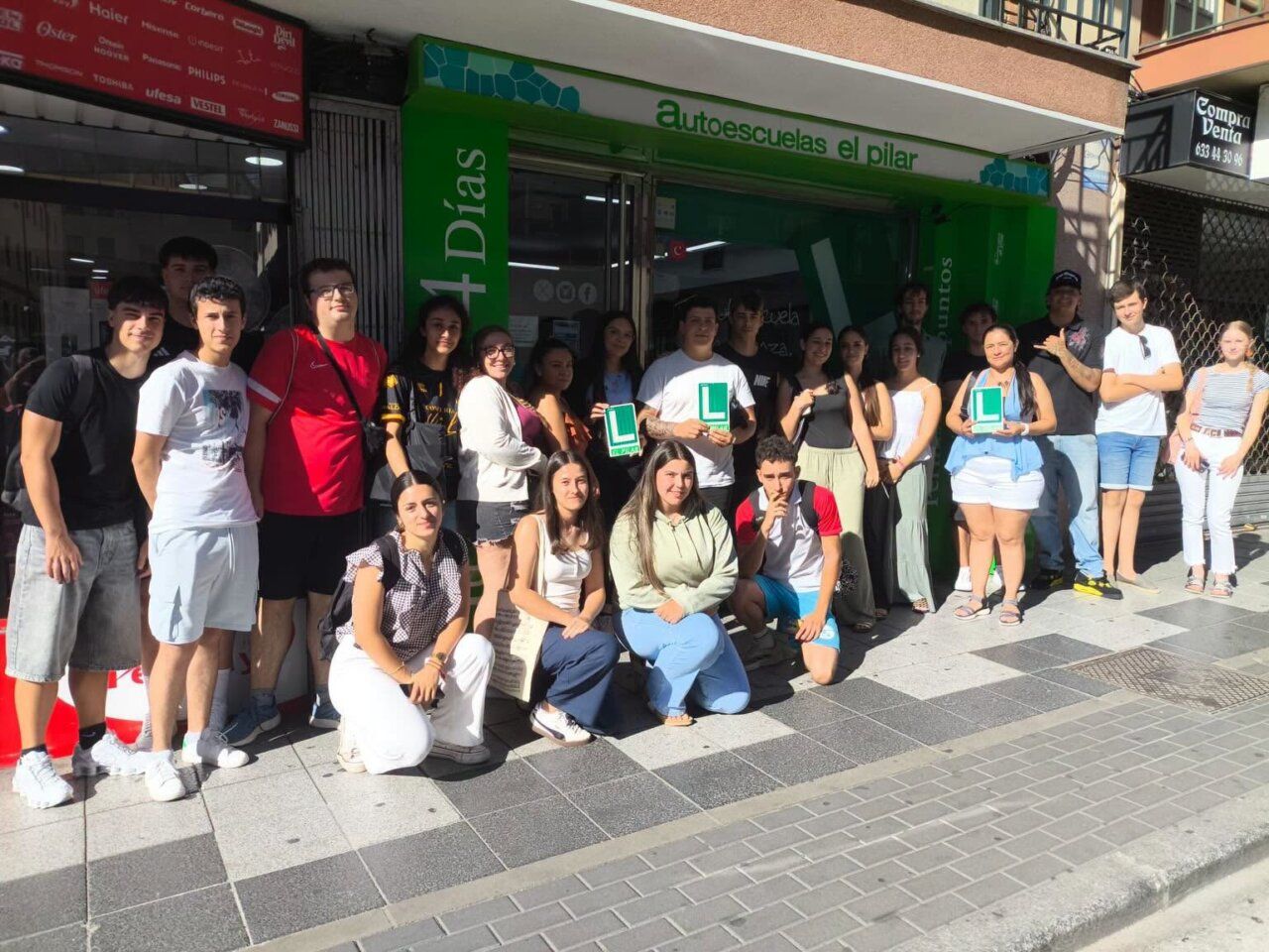 Grupo de estudiantes en Autoescuelas El Pilar sosteniendo carteles de aprendizaje