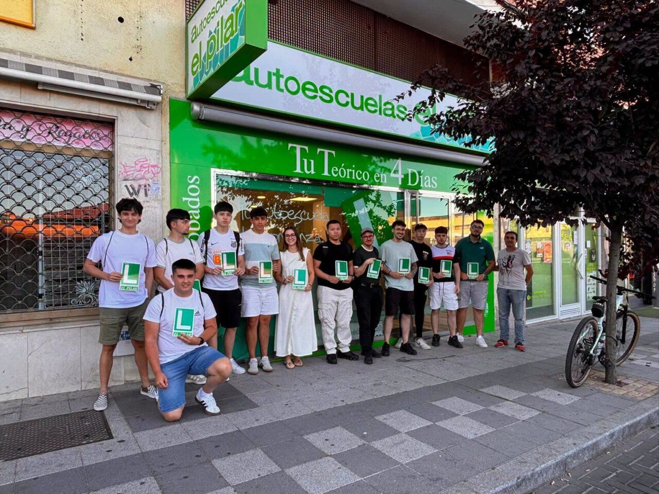 Grupo de estudiantes en Autoescuelas El Pilar sosteniendo carteles de aprendizaje