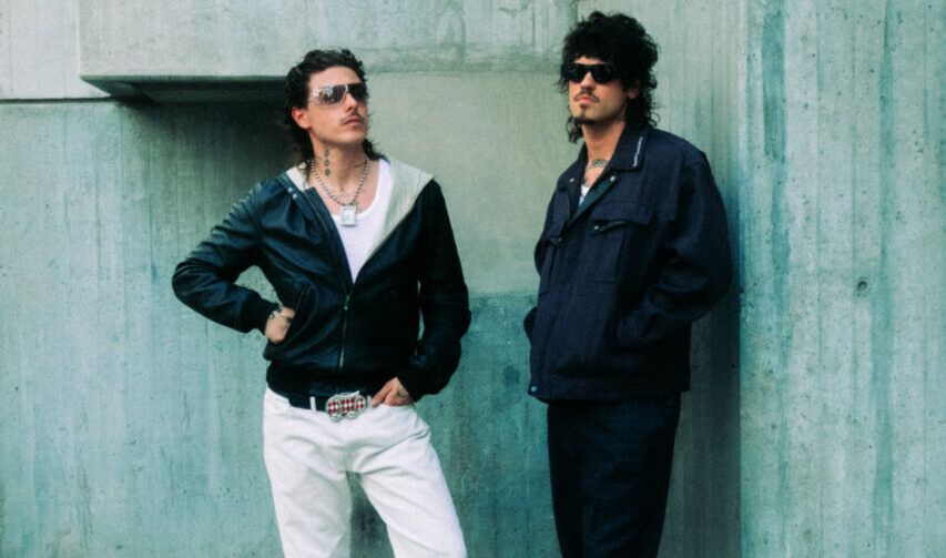 Dos músicos posando frente a una pared de concreto