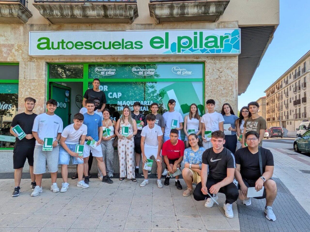 Grupo de estudiantes en Autoescuelas El Pilar sosteniendo carteles de aprendizaje