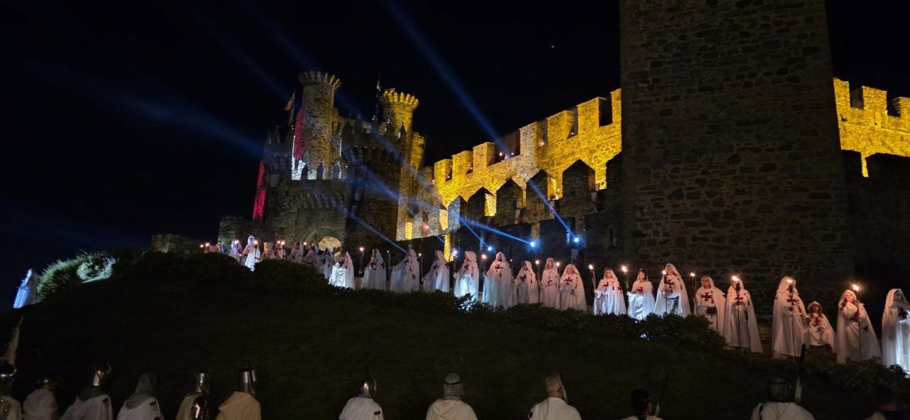 Desfile templario en Ponferrada con participantes en túnicas blancas y castillo iluminado