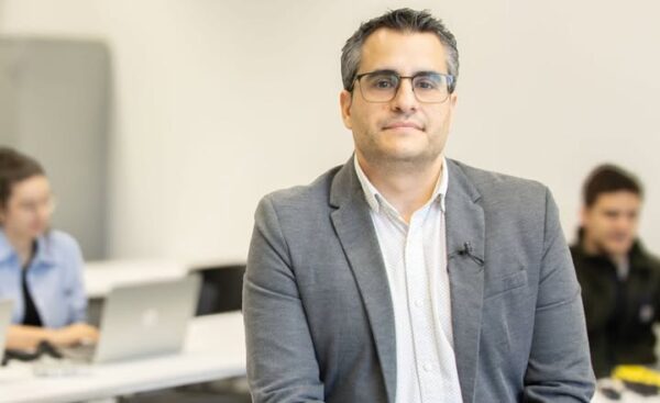 Profesor Javier Parra sentado en un aula con estudiantes al fondo