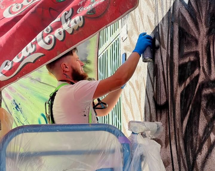 Muralista pintando en la calle bajo una sombrilla