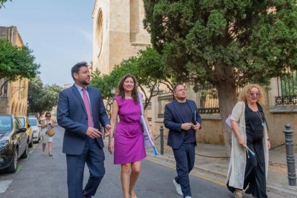 Grupo de personas caminando en una calle con árboles y edificios históricos.
