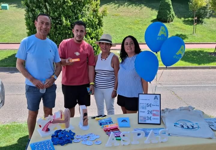 Grupo de personas en evento benéfico con mesa de ASPAS y globos azules