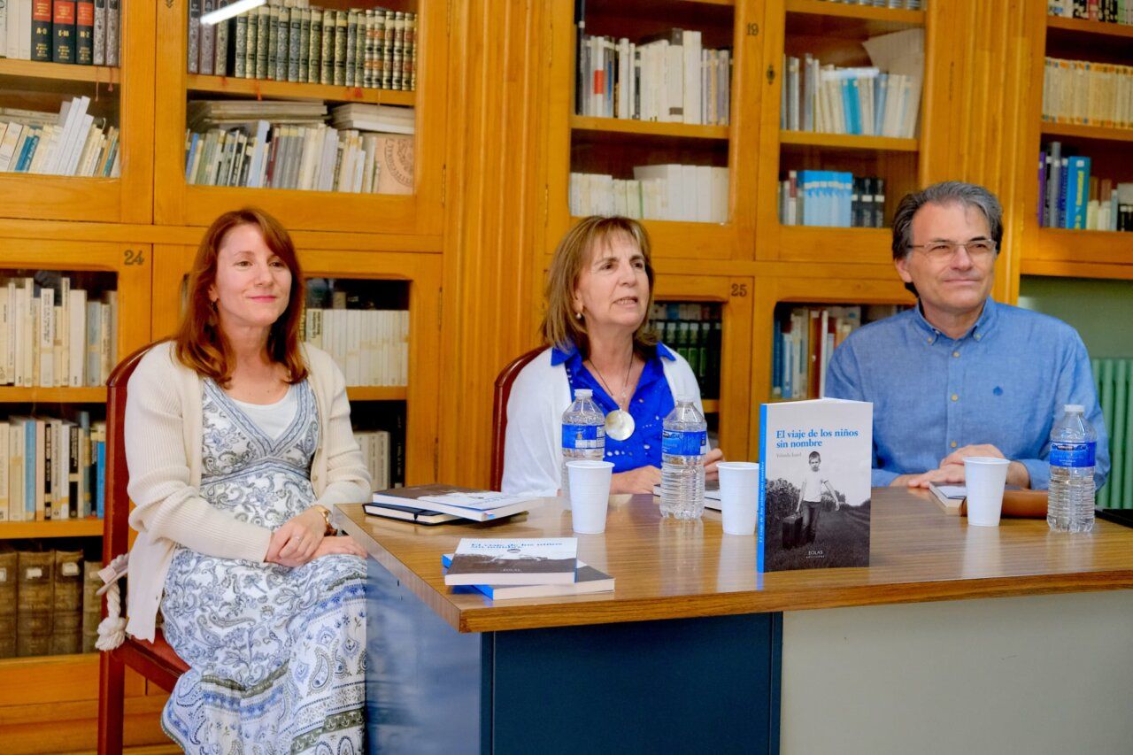 Tres personas sentadas en una mesa con libros y botellas de agua en una biblioteca