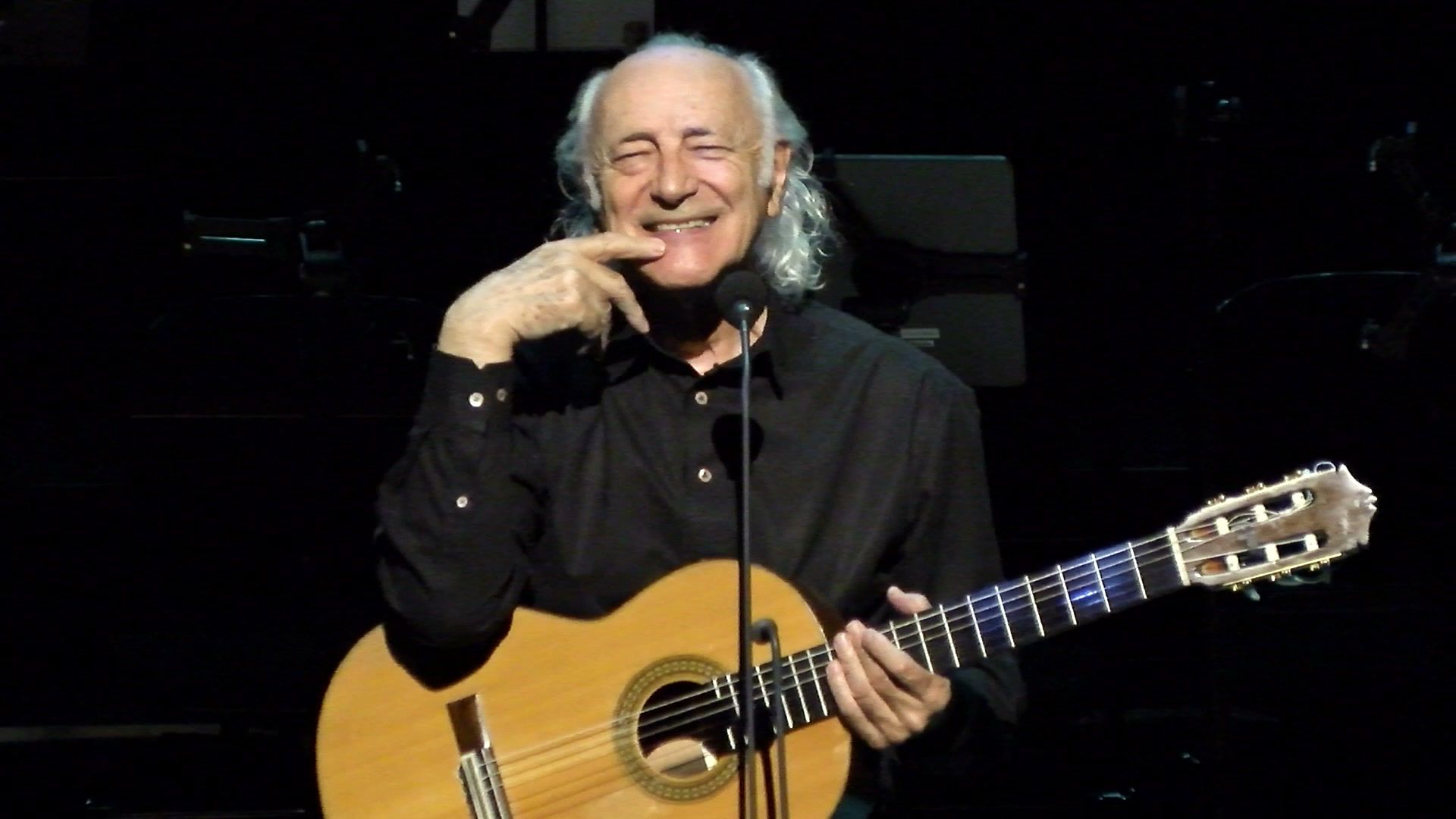 Amancio Prada sonriendo mientras toca la guitarra en un concierto