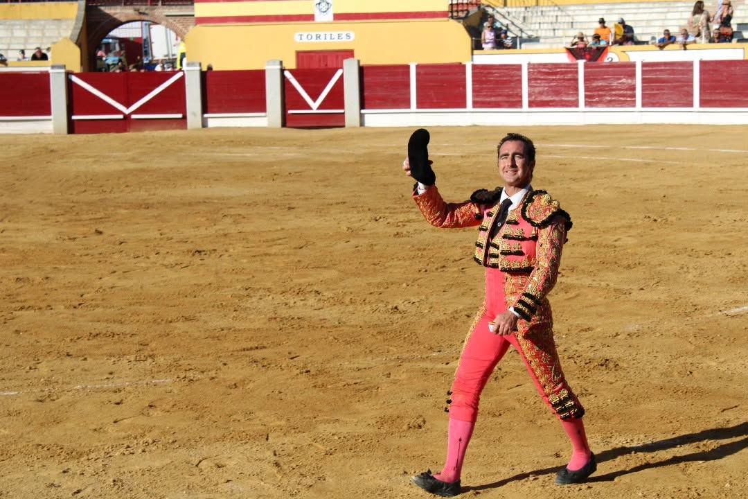 Torero vestido de luces en la plaza de toros, levantando un sombrero.
