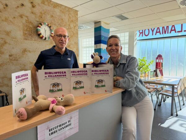 Dos personas en la biblioteca de Villamayor con libros y un muñeco de peluche