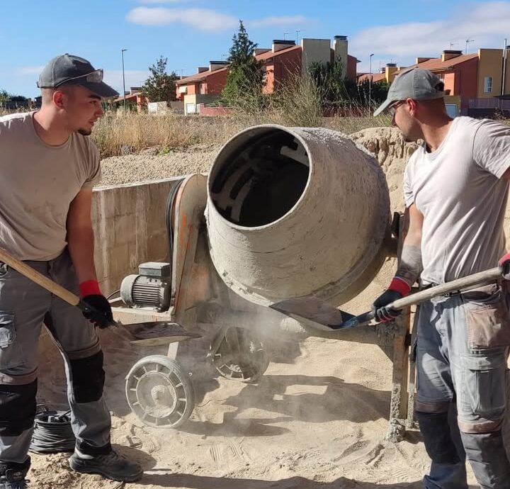 Dos trabajadores utilizando una hormigonera en un sitio de construcción