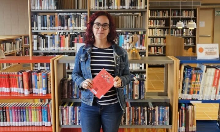 Mujer sosteniendo un libro en una biblioteca con estanterías llenas.