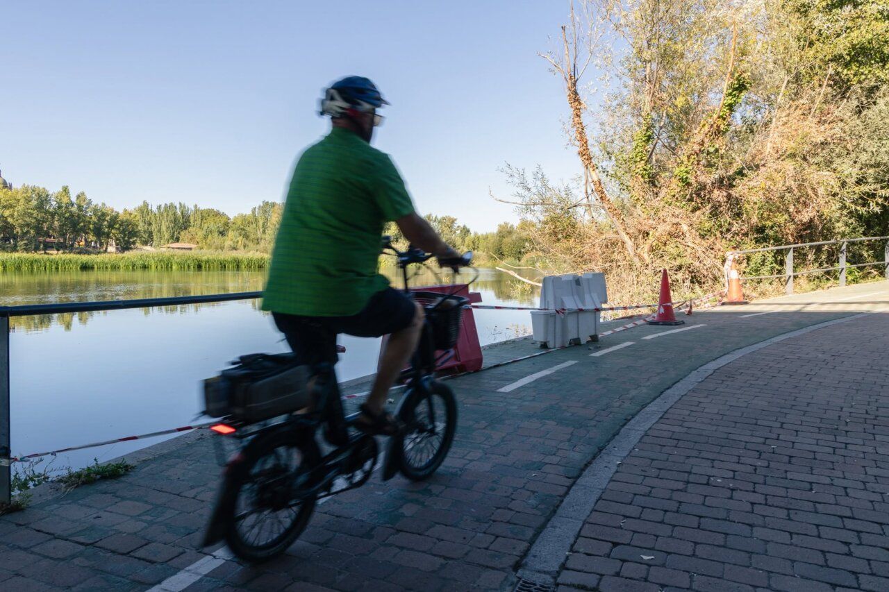 Ciclista en un paseo junto a un río rodeado de vegetación.