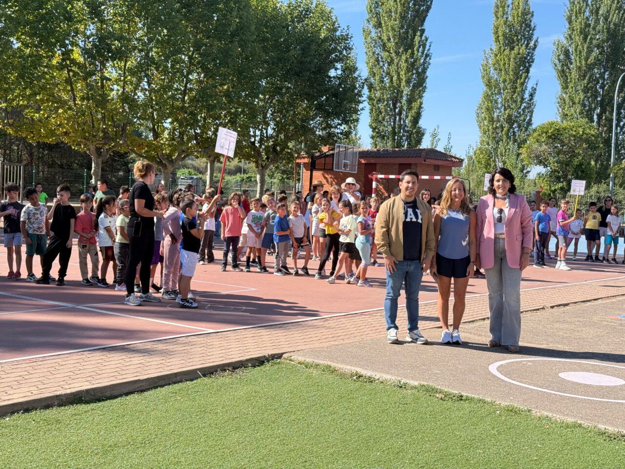 Grupo de niños y adultos en un evento de deporte escolar al aire libre.