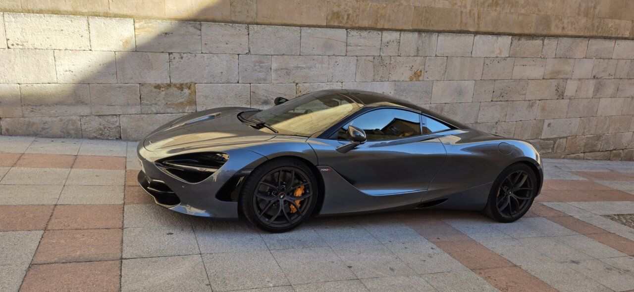 Un McLaren 720S de color gris estacionado frente a una pared de piedra.