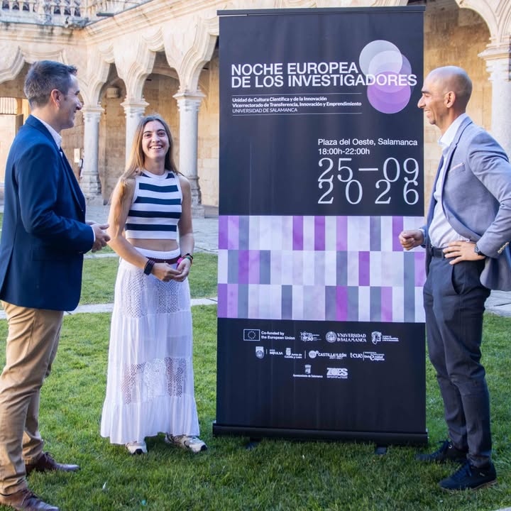Tres personas conversando frente a un cartel de la Noche Europea de los Investigadores en Salamanca.