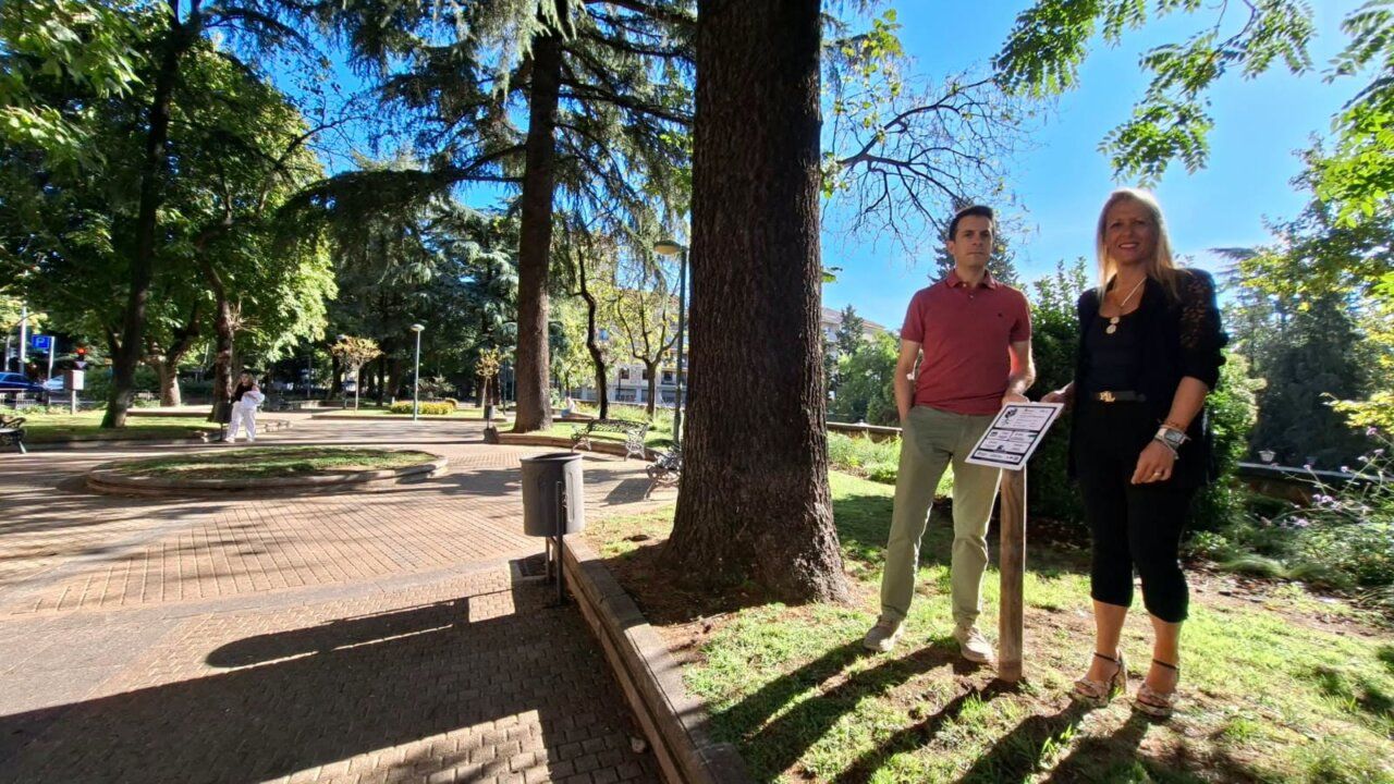 Dos personas en un parque de Salamanca con árboles y etiquetas informativas.