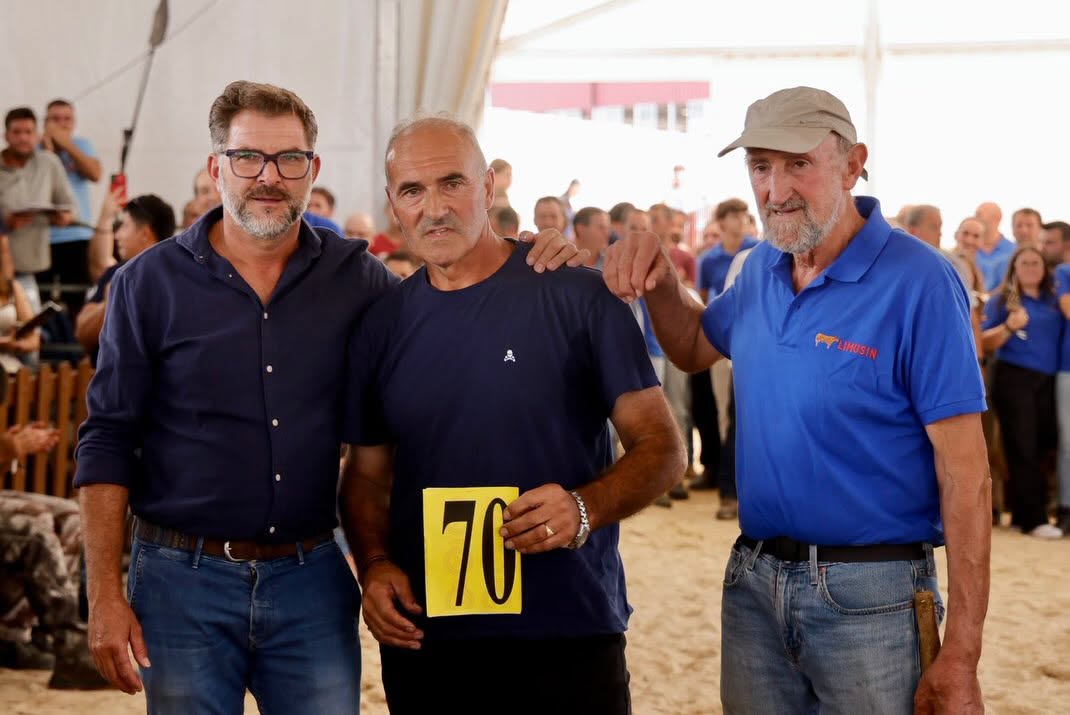 Tres hombres posando en un evento de subasta con un número en la mano
