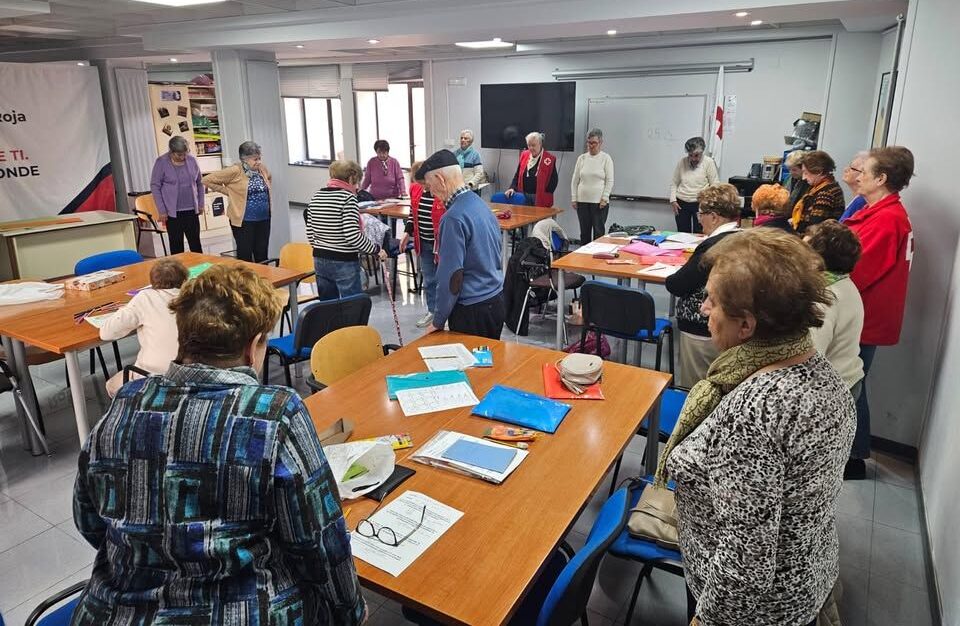 Personas mayores reunidas alrededor de mesas con papeles y materiales en una sala