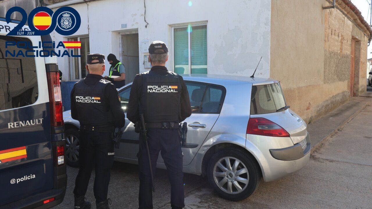 Dos agentes de Policía Nacional junto a un coche plateado y una furgoneta policial.