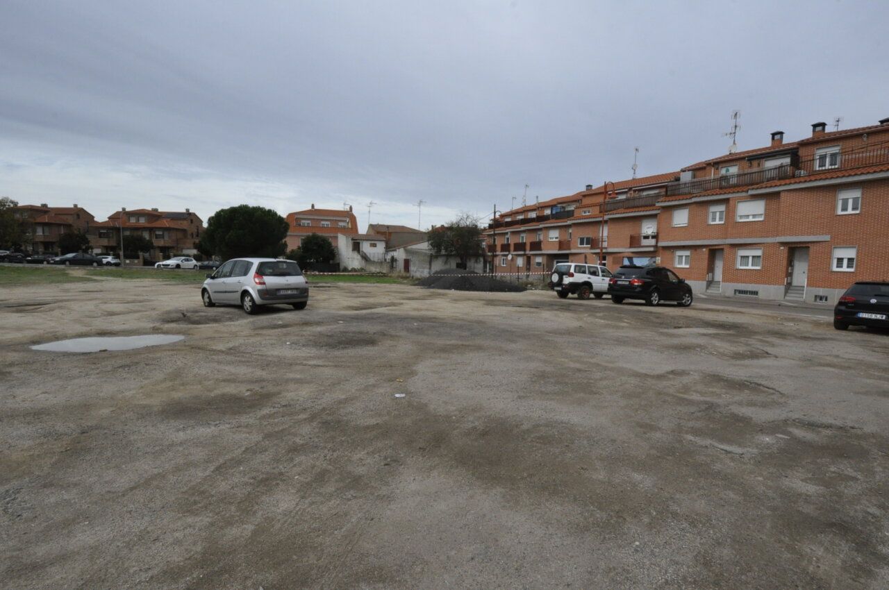 Amplio aparcamiento de tierra con varios coches frente a edificios residenciales de ladrillo