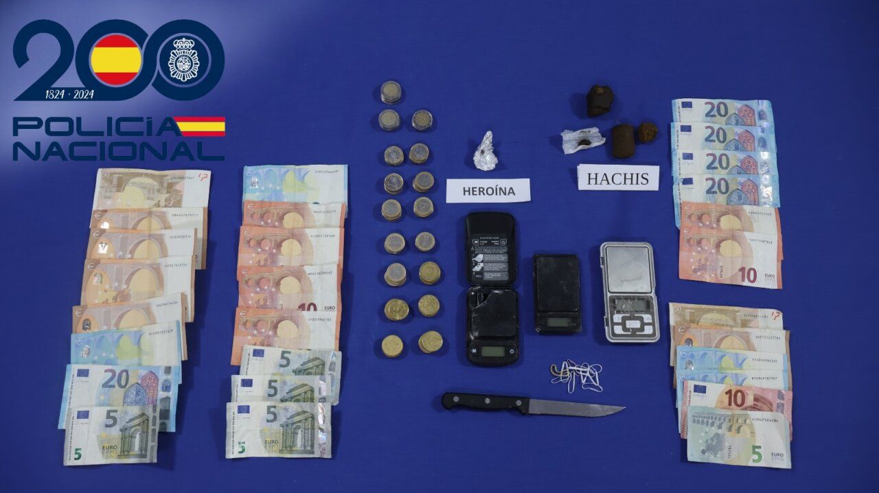 Dinero, monedas, básculas y otros objetos expuestos sobre un fondo azul junto al logotipo policial.