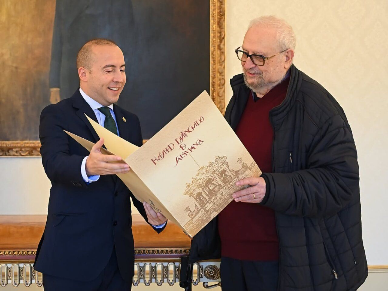 Dos hombres sostienen un gran documento con la inscripción Huésped Distinguido Salamanca