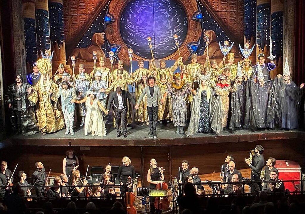 Elenco de ópera sobre el escenario, con músicos de la orquesta en el foso.