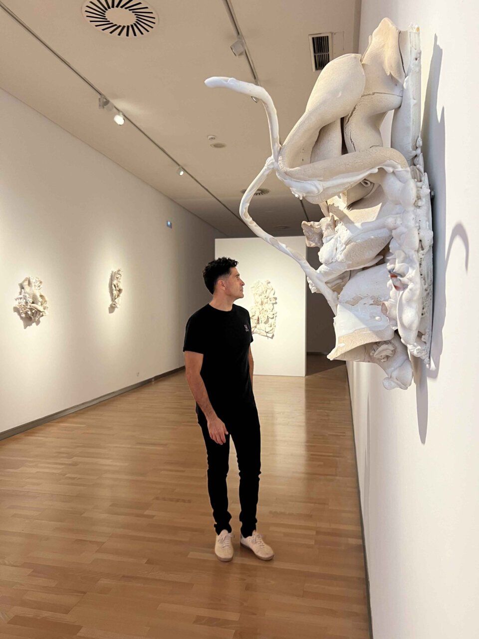 Una persona observa una gran escultura blanca en relieve en una sala de exposición.