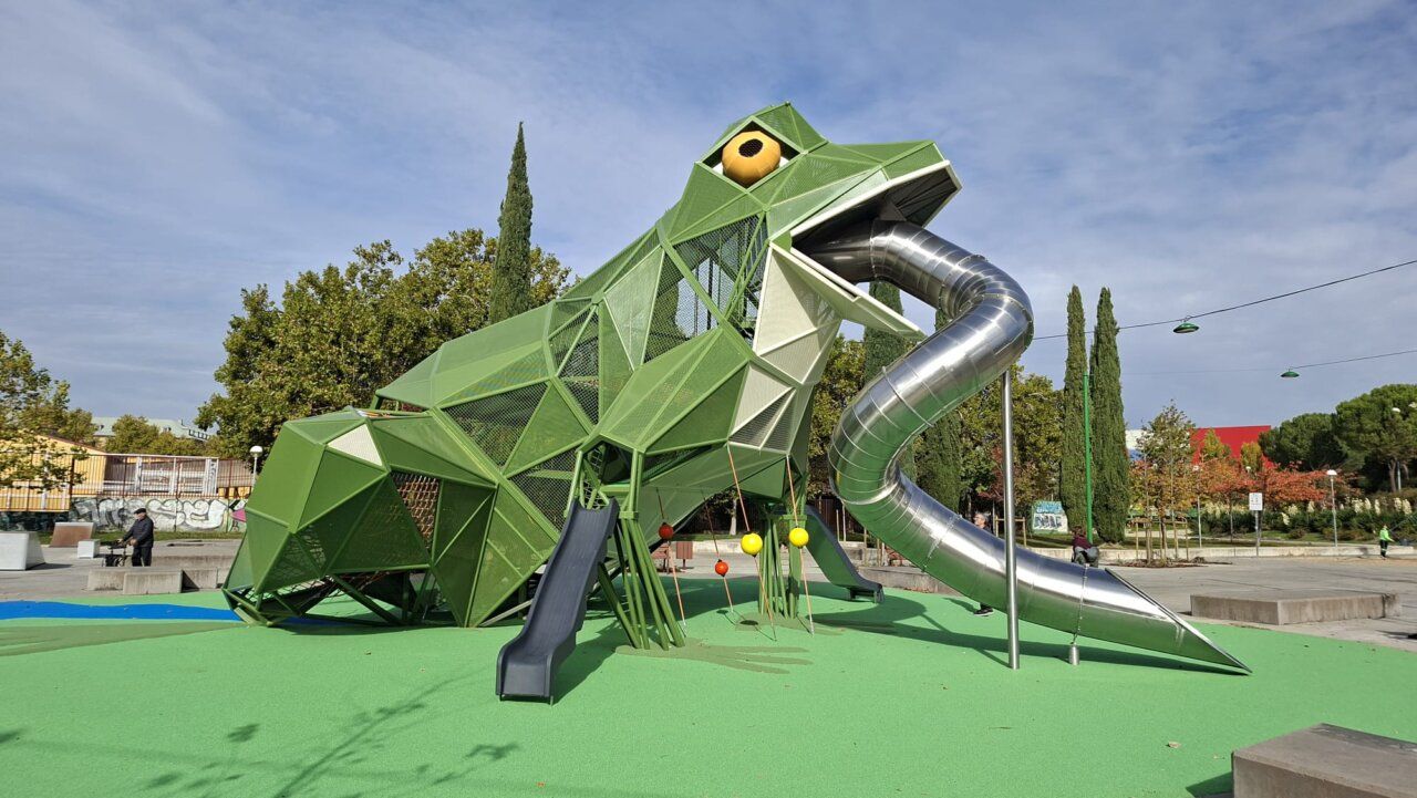 Estructura verde de juego con forma de rana y toboganes en un parque