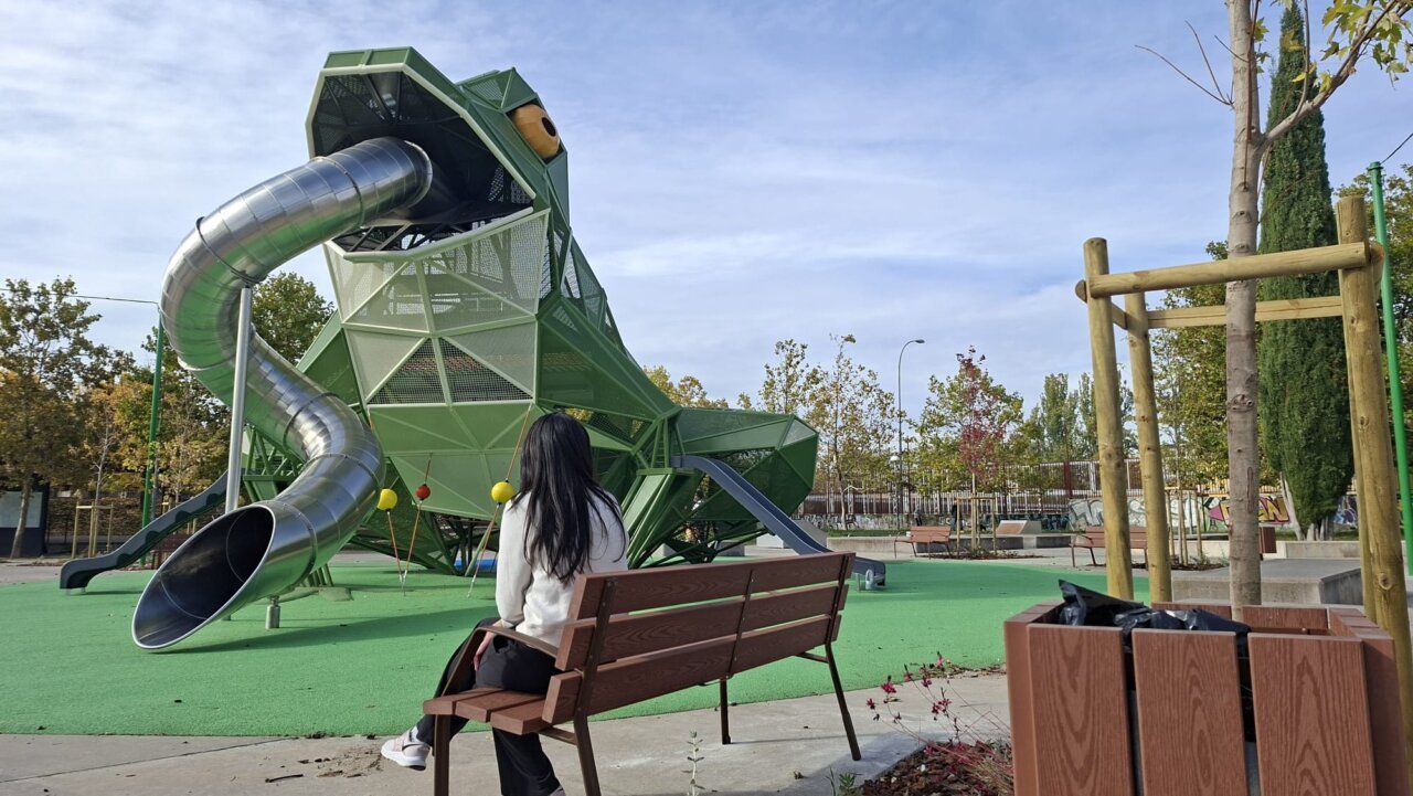 Estructura de juego verde con forma de rana y tobogán en un parque