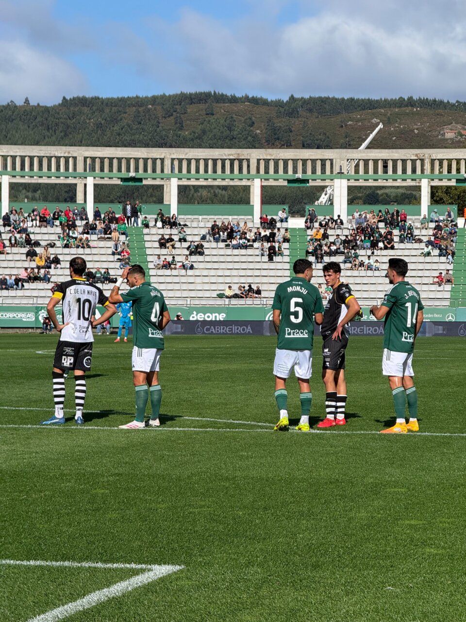 Futbolistas de verde y blanco y de negro esperan una acción en el campo