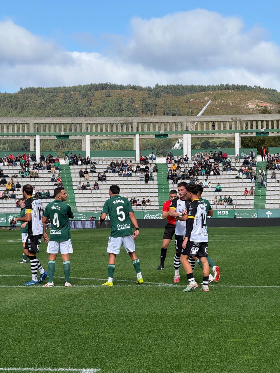 Futbolistas de verde y blanco y de camiseta oscura se agrupan sobre el césped.