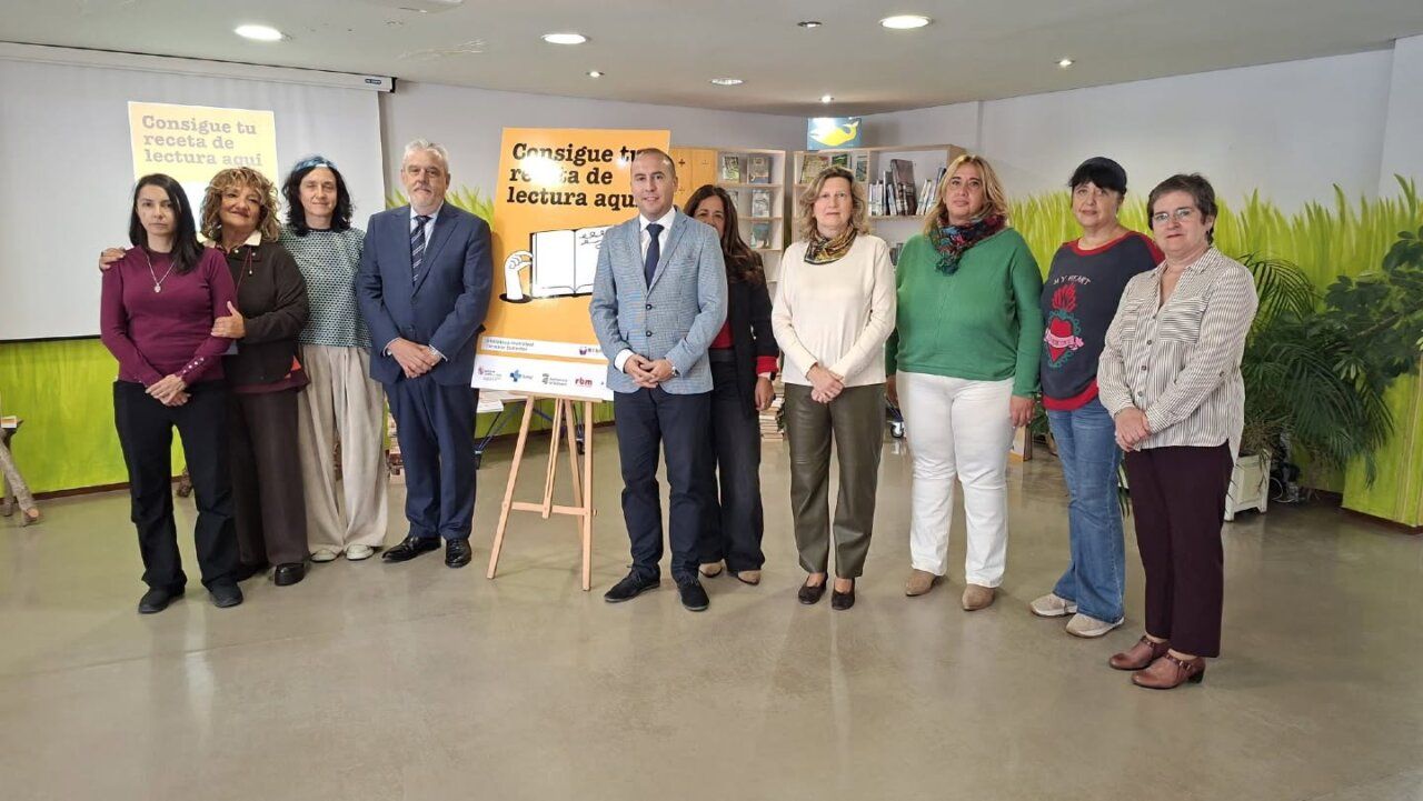 Grupo de personas posa junto a carteles de una iniciativa de lectura y una estantería de libros
