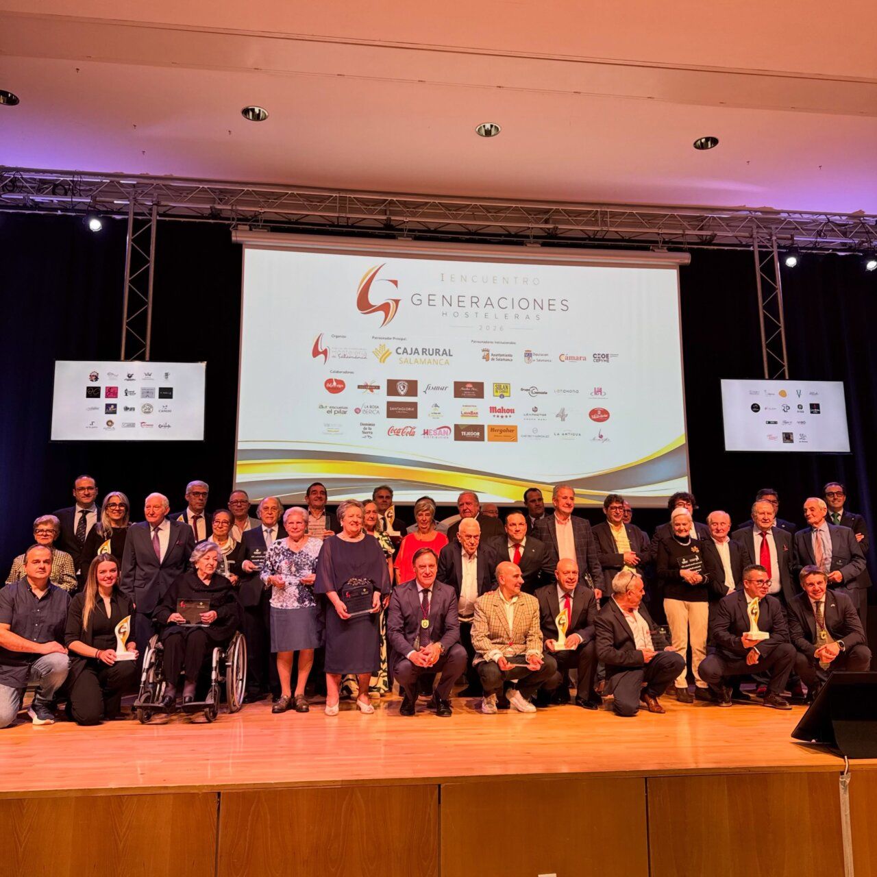 Grupo de personas en un escenario bajo una pantalla del Encuentro de Generaciones Hosteleras