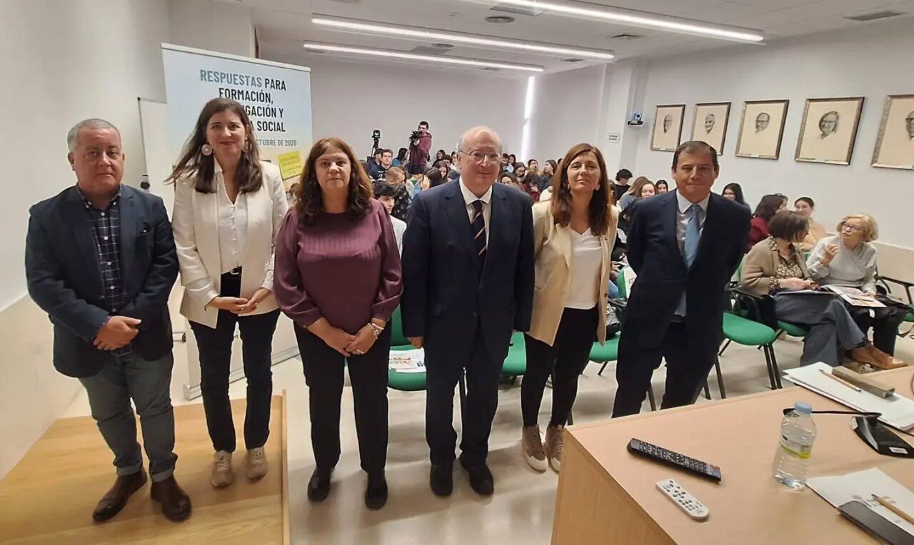 Seis personas posan ante el público en una sala con un cartel sobre formación e investigación.