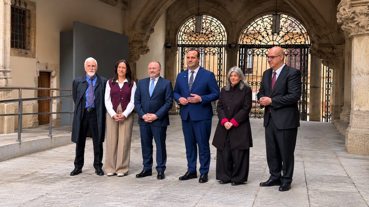 Seis personas posan en un patio de piedra ante unas puertas de hierro ornamentadas.