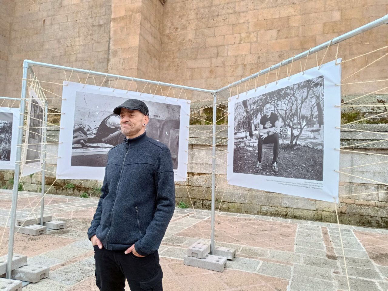 Un hombre posa delante de varias fotografías en blanco y negro expuestas al aire libre.