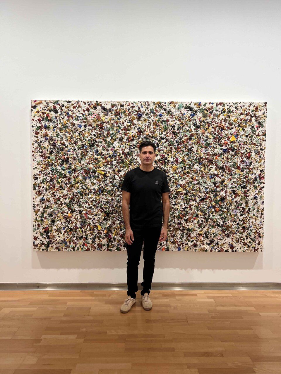 Un hombre vestido de negro frente a una gran obra abstracta de textura multicolor