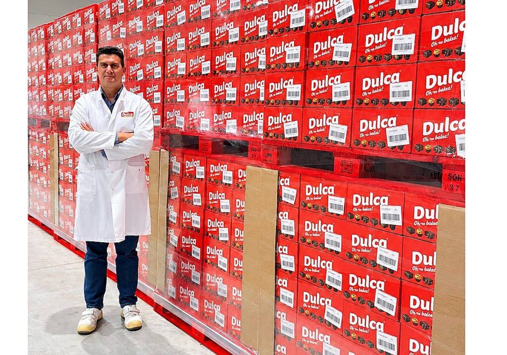 Hombre con bata blanca junto a una gran pila de cajas rojas de Dulca