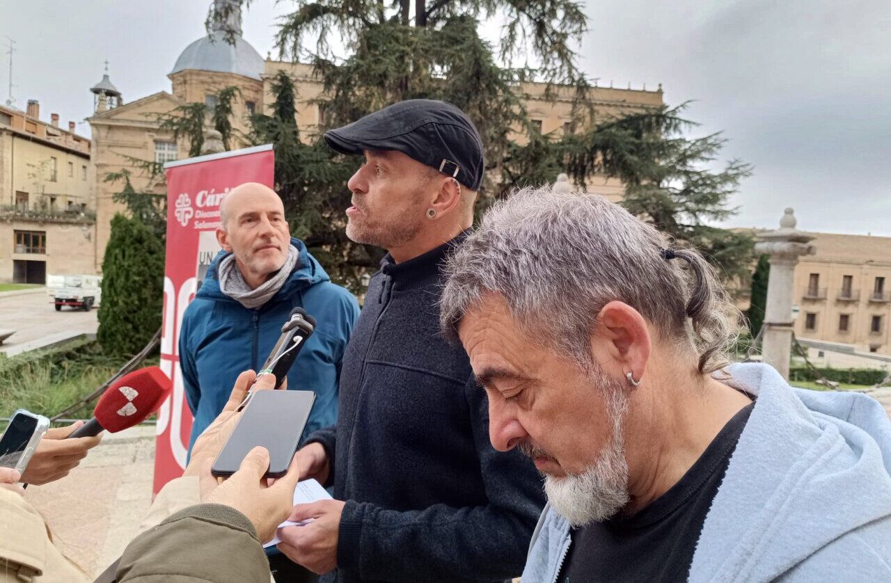 Tres hombres durante una atención a medios, con micrófonos y un cartel de Cáritas.