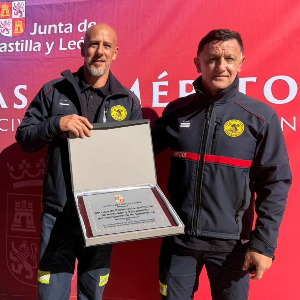 Dos hombres con uniformes oscuros muestran una placa dentro de un estuche abierto.