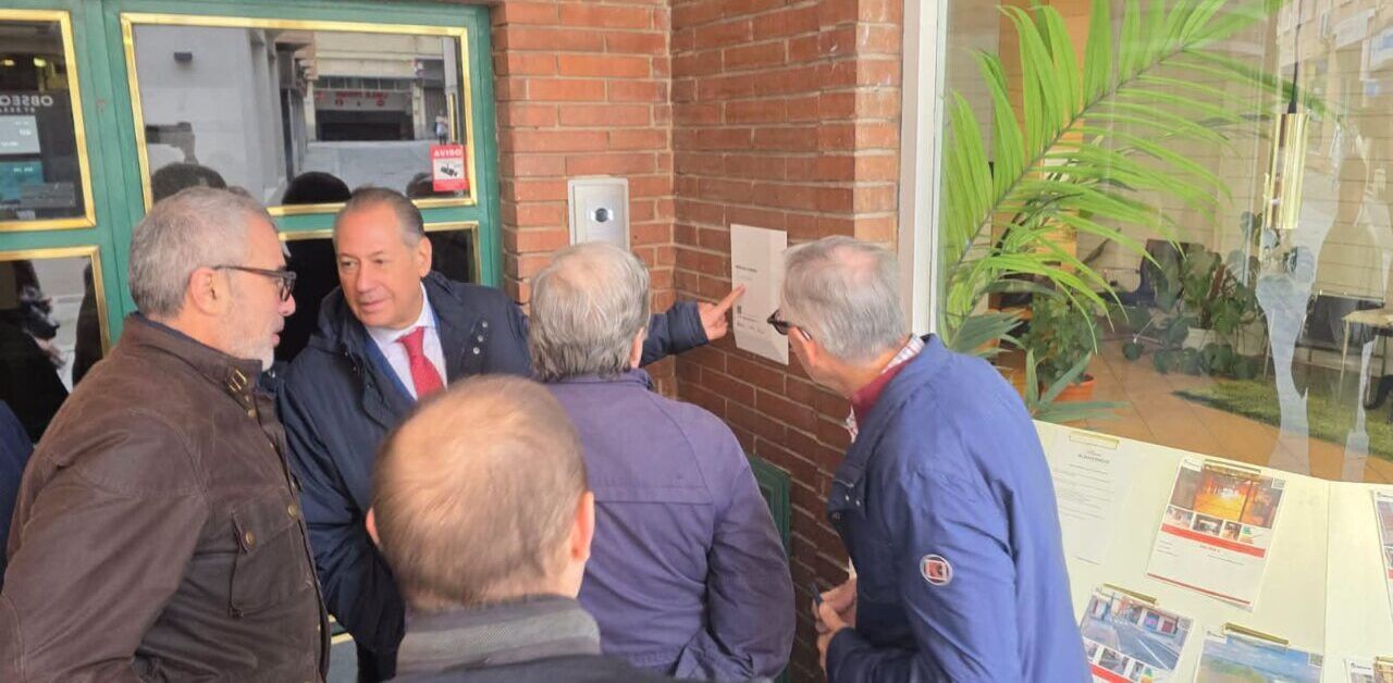 Fotografía de varios hombres observando una placa en una pared de ladrillo.
