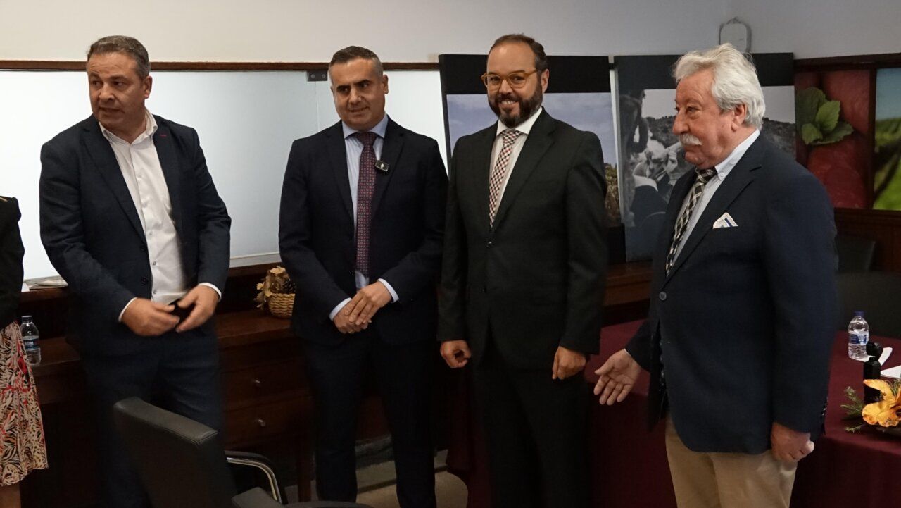 Cuatro hombres están de pie en una sala con paneles y mobiliario al fondo