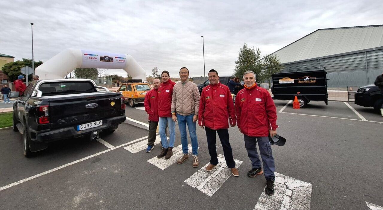 Cinco hombres posan junto a vehículos y el arco del Spain Classic Raid.