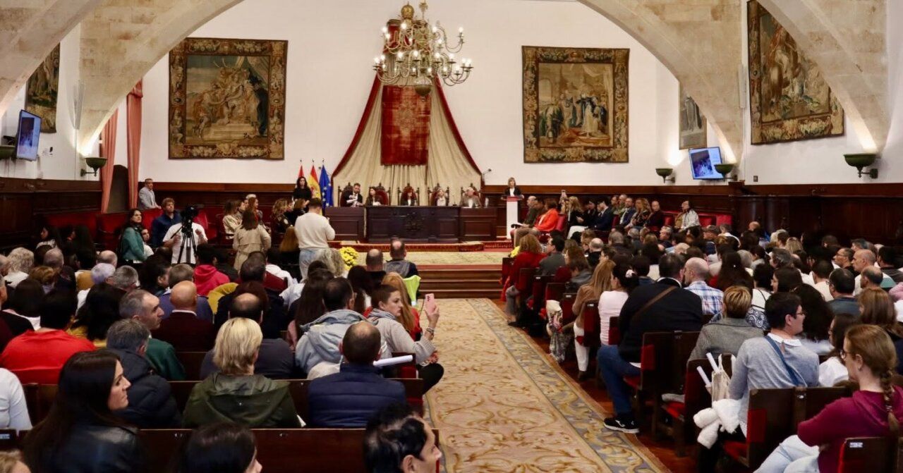 Público sentado frente a una mesa presidencial en un salón histórico de actos