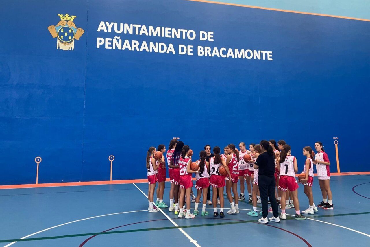 Grupo de jugadoras de baloncesto reunidas con balones en una pista cubierta