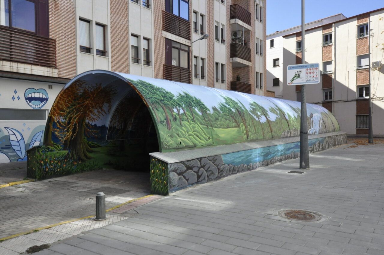 Túnel urbano decorado con un mural de árboles, vegetación y un arroyo.