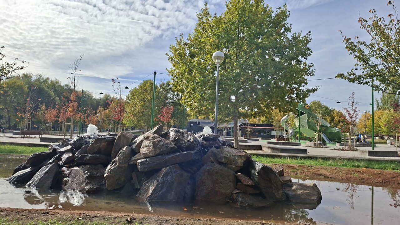Rocas de una fuente en primer plano y estructura verde de juegos en un parque.