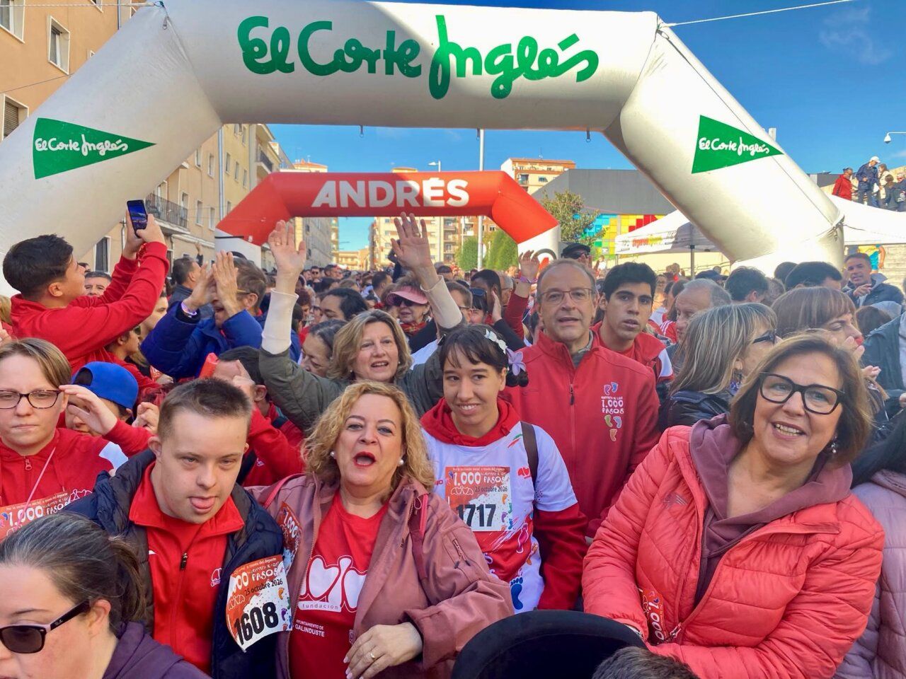 Una multitud con dorsales se reúne bajo un arco de salida en una carrera.